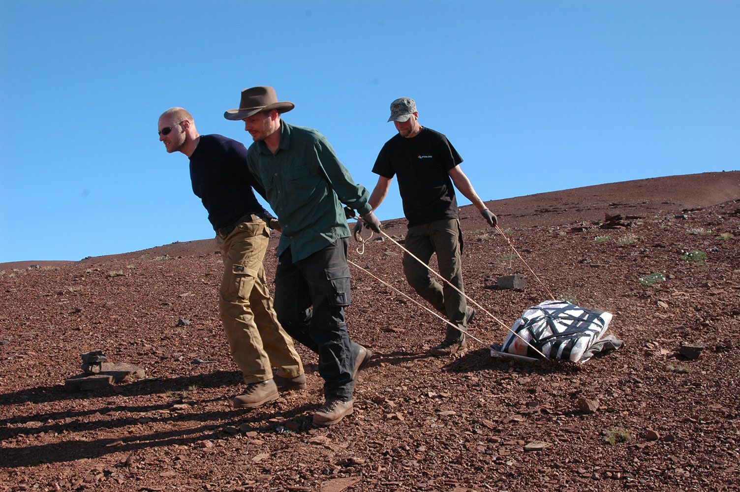 Fotografi fra Grønland, hvor tre mænd slæber stenblokke med knogler